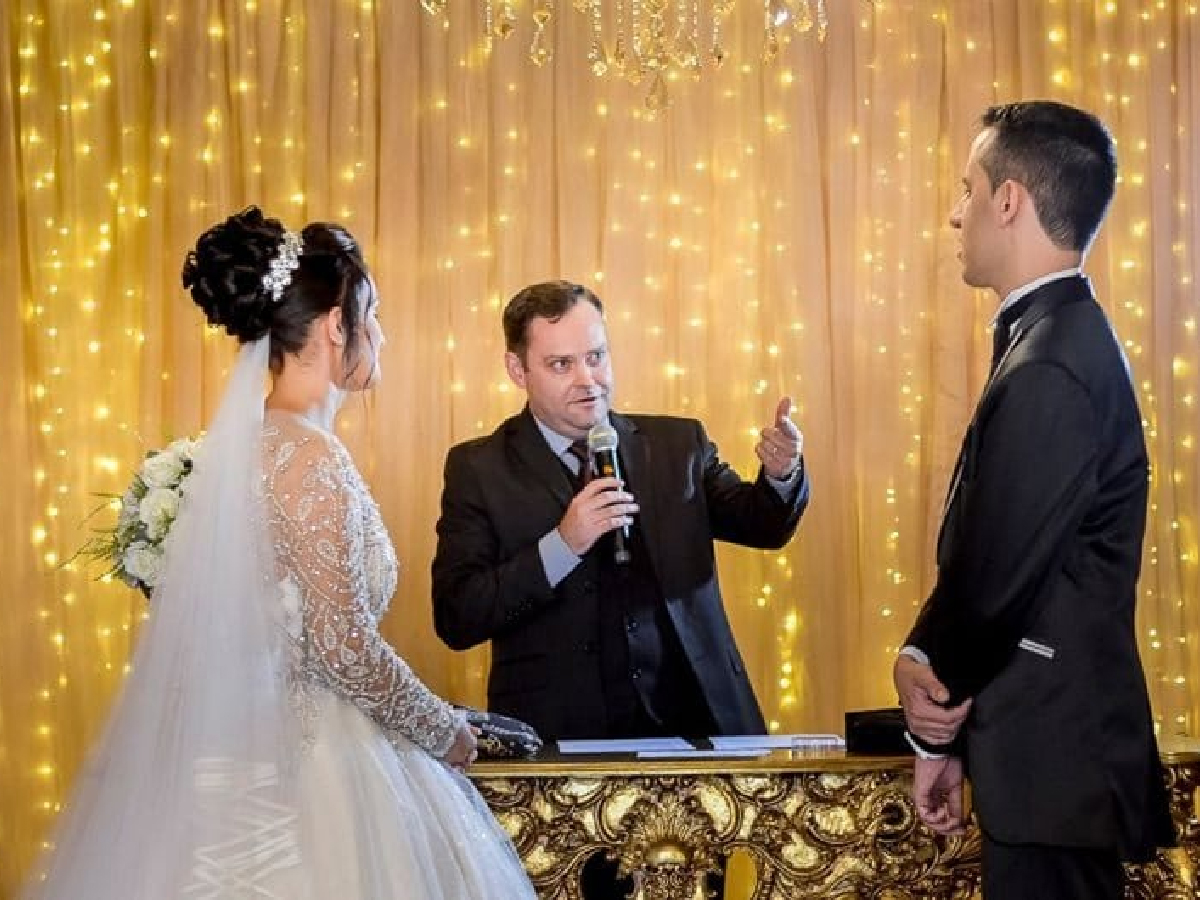 Camilo Lelles celebrando casamento com microfone no altar, noivos ao lado
