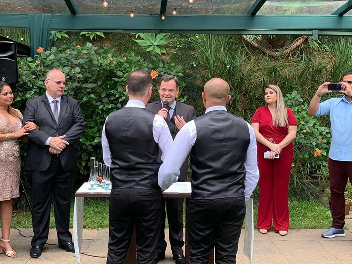 Celebrante Camilo Lelles conduzindo cerimônia de casamento ao ar livre para dois noivos