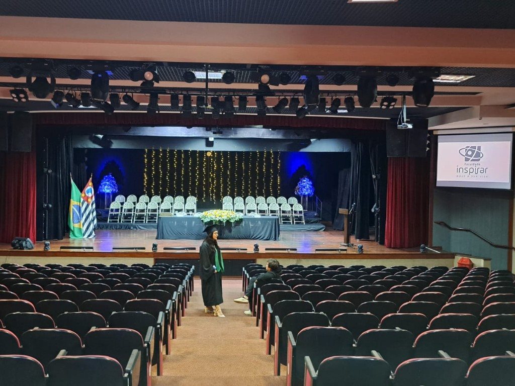 Colação de grau em auditório com formanda no corredor e palco preparado