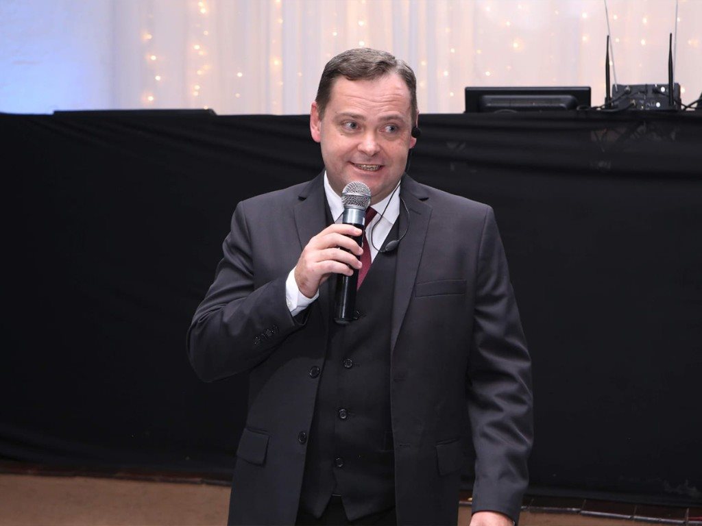 Camilo Lelles como mestre de cerimônia em evento corporativo com microfone