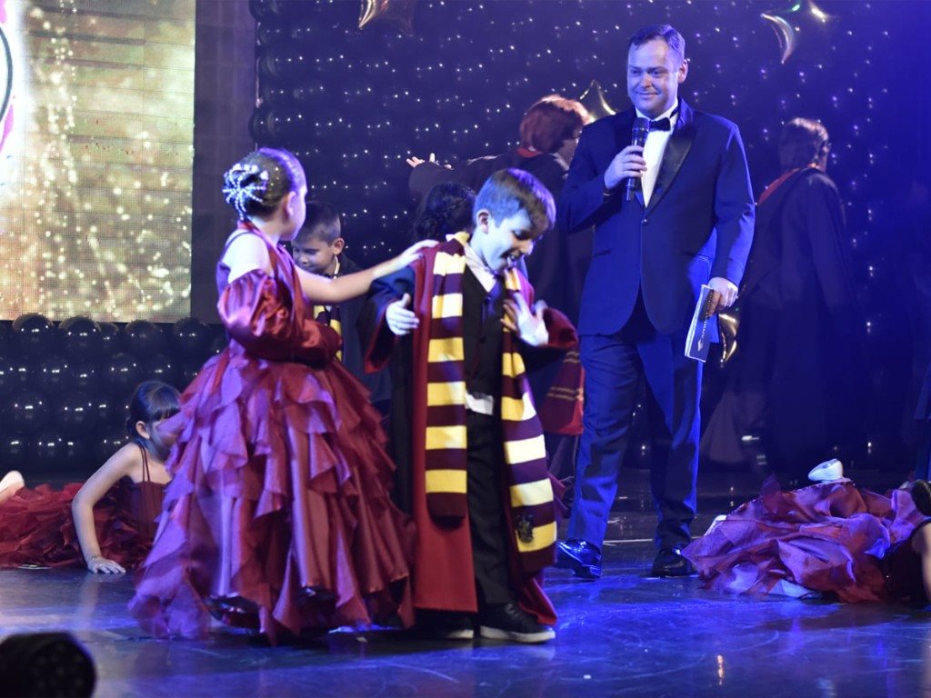 Camilo Lelles conduzindo formatura infantil no palco com crianças e microfone
