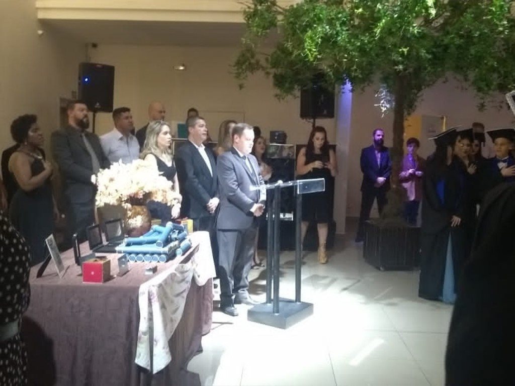 Camilo Lelles na colação de grau com formandos, diplomas e arranjo de flores